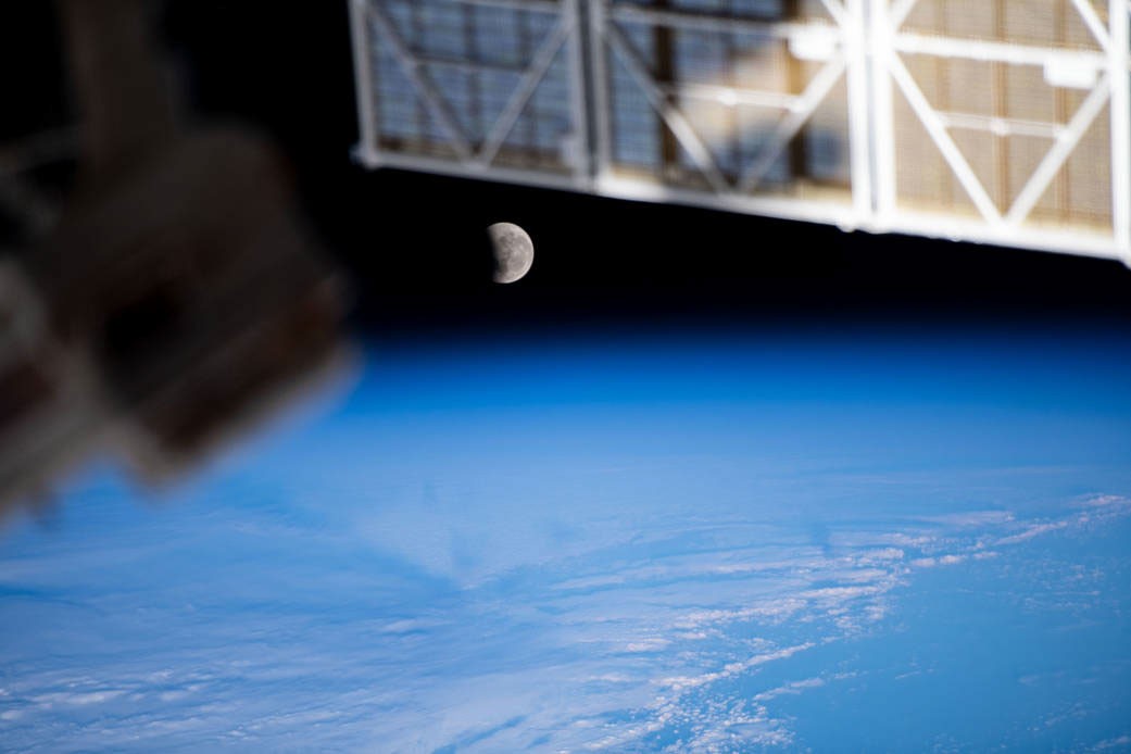 A partly eclipsed Moon above Earth’s blue horizon, photographed from the International Space Station